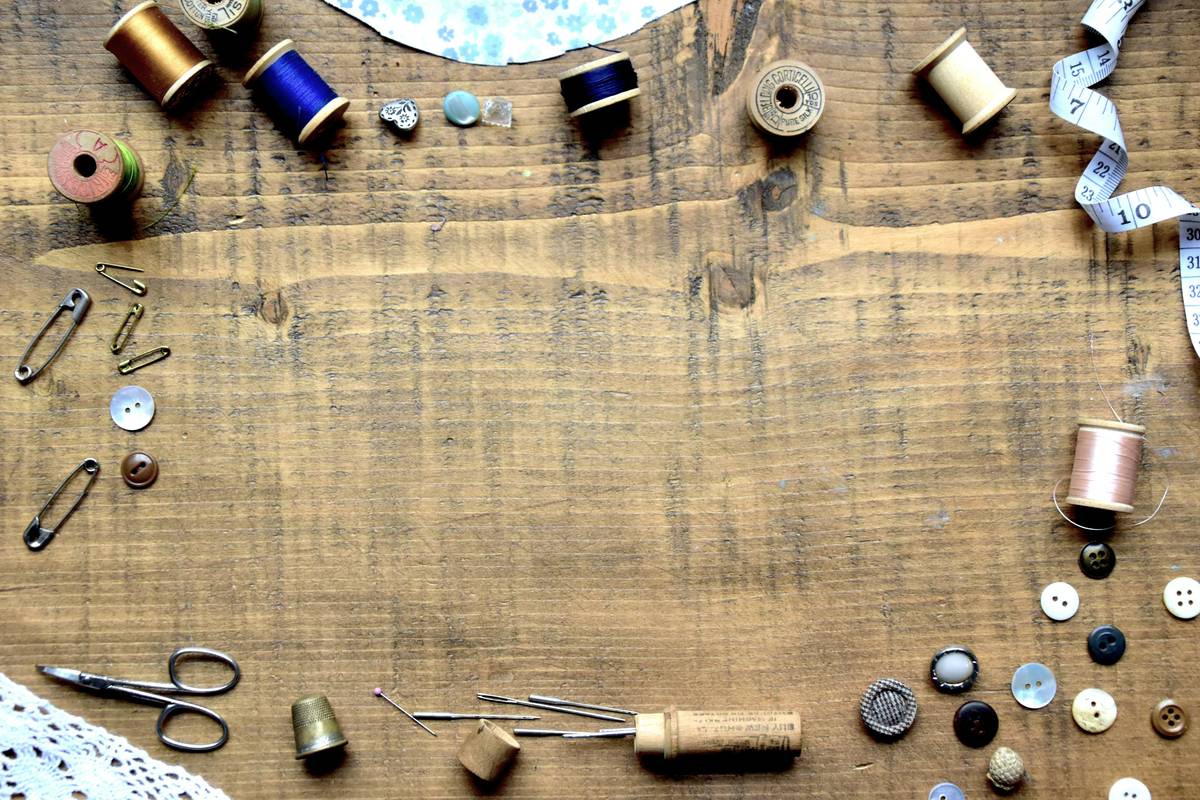how to make homemade placemats: hands sewing fabric edges on a wooden table with scissors and measuring tape nearby